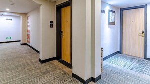 A hotel corridor with a carpeted floor, wooden doors, and a wall-mounted sign.