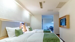 A hotel room with two beds, a TV mounted on the wall, and a desk in the background.