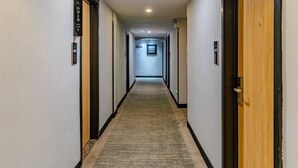 A hotel hallway with carpeted floors, wooden doors, and signs indicating room numbers.
