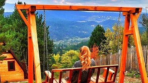 A wooden swing set overlooking a scenic landscape with a view of distant hills and a cloudy sky.