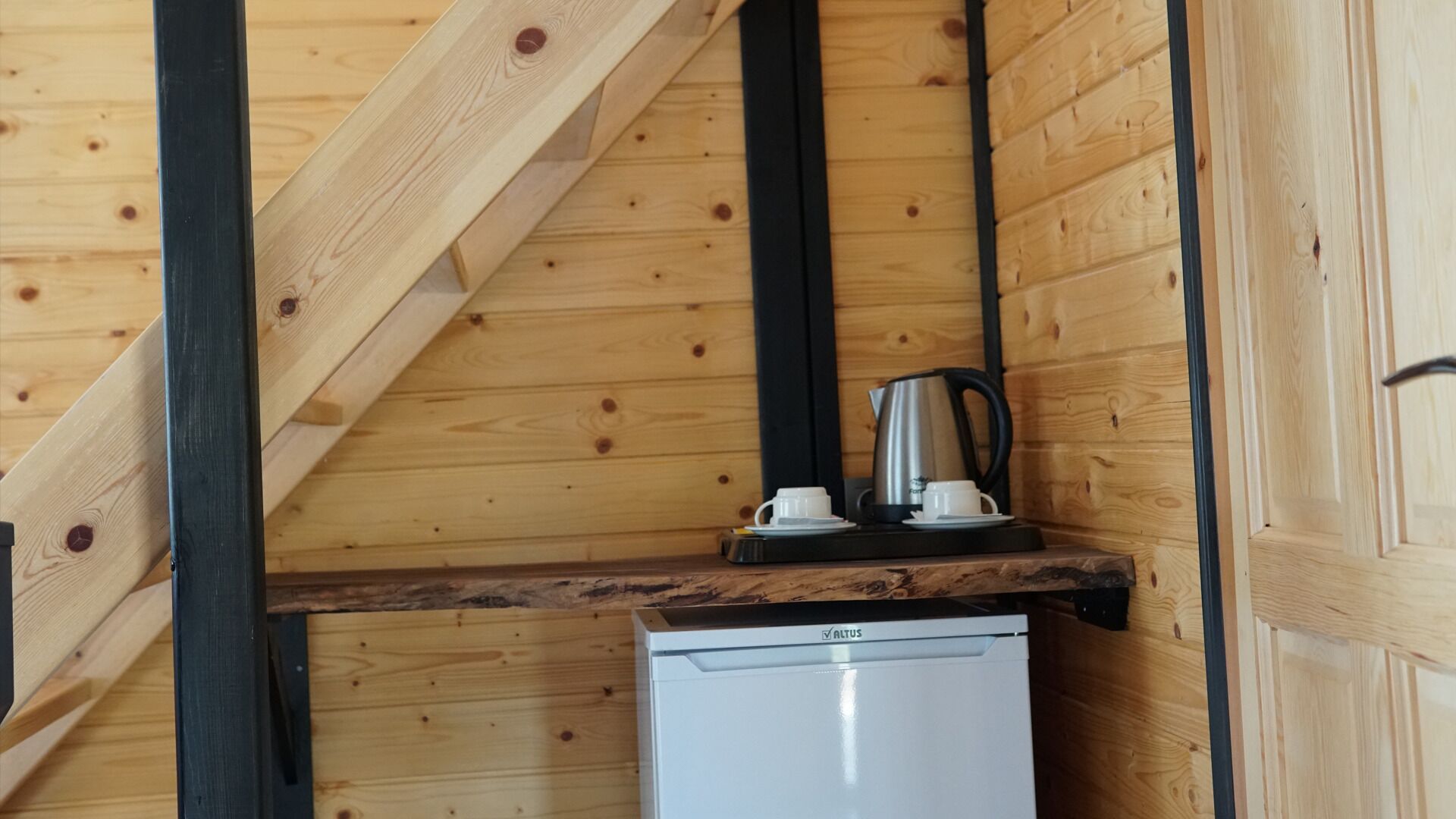 A compact kitchenette with a small white refrigerator, a coffee maker, and a cup on the counter.