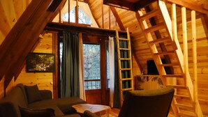 A cozy wooden cabin interior with a loft bed, a sofa, and a table.