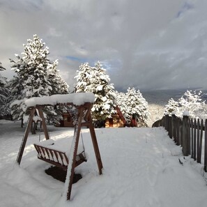 A snow-covered swing set in a backyard with a wooden fence and snow-laden trees. - Fikri Atalay Konağı (Mengen)