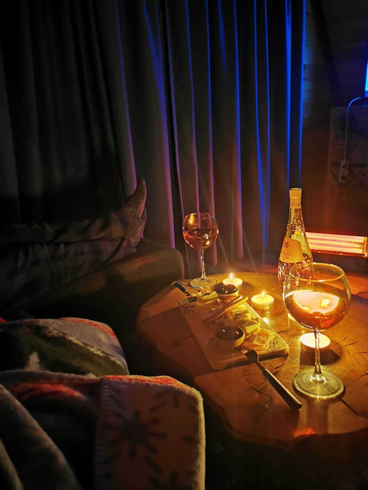 A cozy room with a wooden table set for a meal, featuring a candle, a bottle, and a glass of wine.