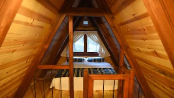An attic bedroom with a wooden sloped ceiling, a bed with striped bedding, and a window with curtains.