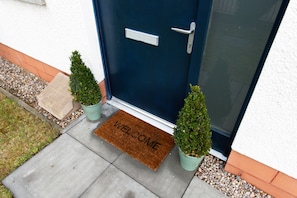 Welcome to a charming entrance with a dark blue door, silver handle, and a warm doormat.