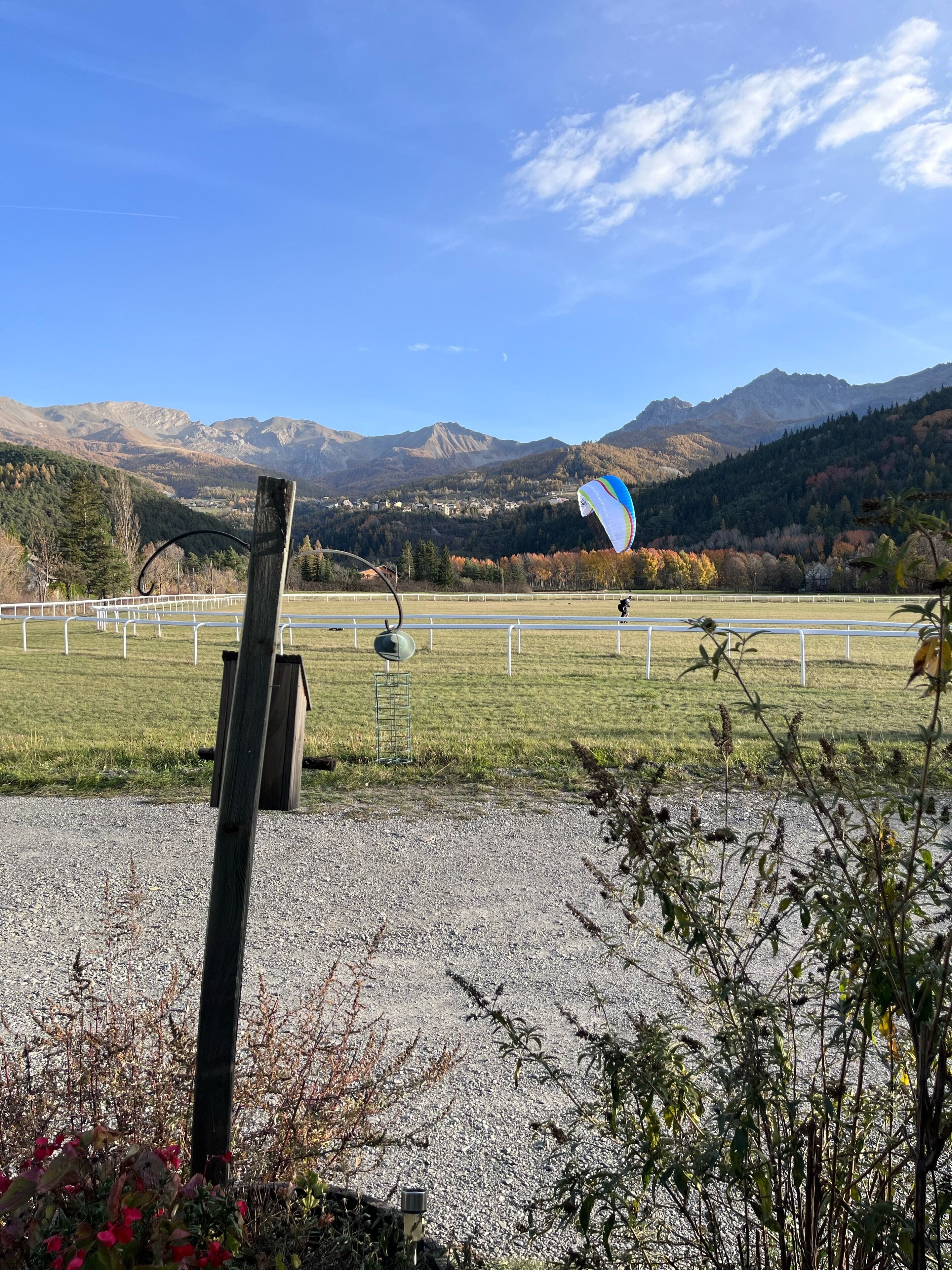 A grassy field with a kite flying, a wooden post, and a mountain range in the background.