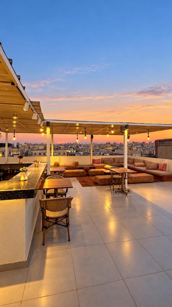 Terraza en la azotea con zona de bar, asientos y vista panorámica de la ciudad al atardecer.
