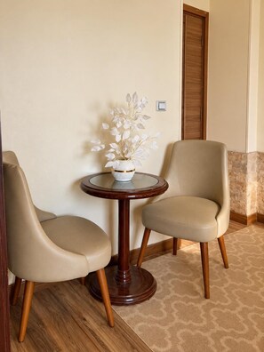 Una habitación con dos sillas color beige, una mesa redonda de madera con un jarrón blanco, y una puerta de madera.