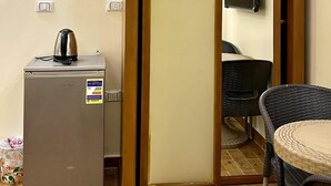 Una habitación compacta con kitchenette, una puerta corredera, un televisor de pantalla plana, una silla de mimbre y una pequeña mesa.
