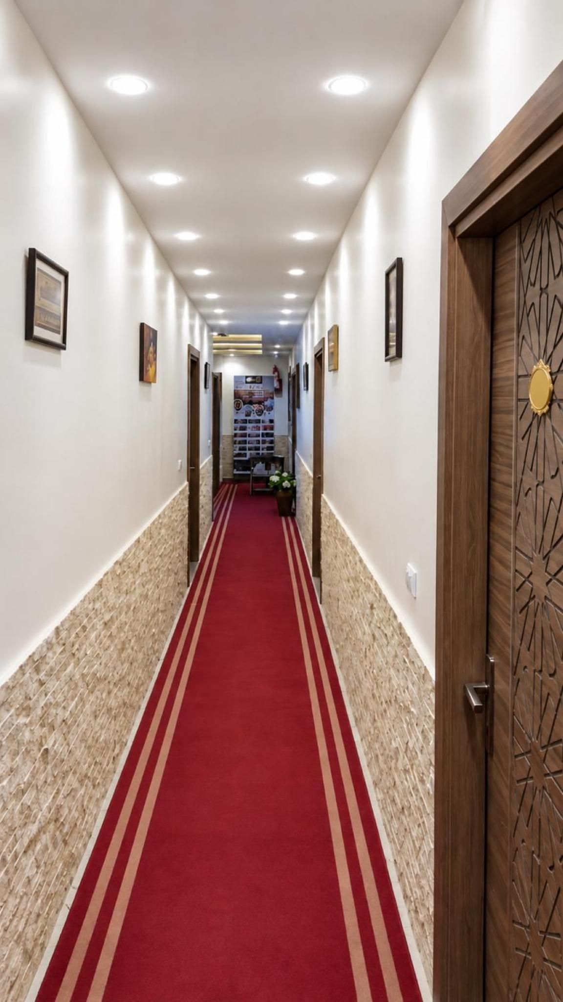 Un pasillo de hotel con alfombra roja, puertas de madera y cuadros en las paredes.