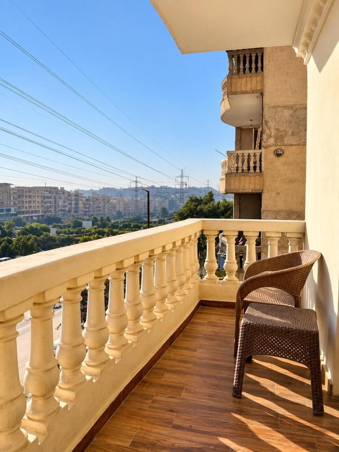 Un balcone con pavimento in legno, una sedia in vimini e vista sulla città.