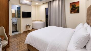 A hotel room with a bed, a bathroom, a TV, and a painting on the wall.