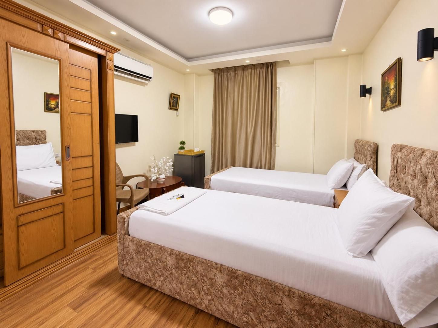 Habitación de hotel con dos camas, un escritorio, una silla, un televisor y un aire acondicionado.