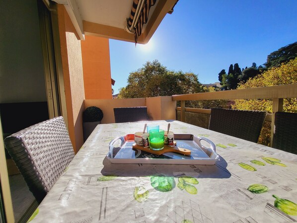 An outdoor dining area with a table set for two, featuring a tablecloth with leaf patterns, a tray with food and drinks, and wicker chairs.