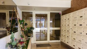 Un ingresso di un hotel con porta in vetro, una fila di armadietti a destra e diverse piante in vaso lungo la parete sinistra.