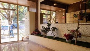 Un'area reception di un hotel con pavimento piastrellato, una scrivania della reception e un vaso a forma di bicicletta con fiori.