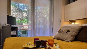 Un letto con un vassoio per la colazione, una televisione e vista sul verde all'esterno.