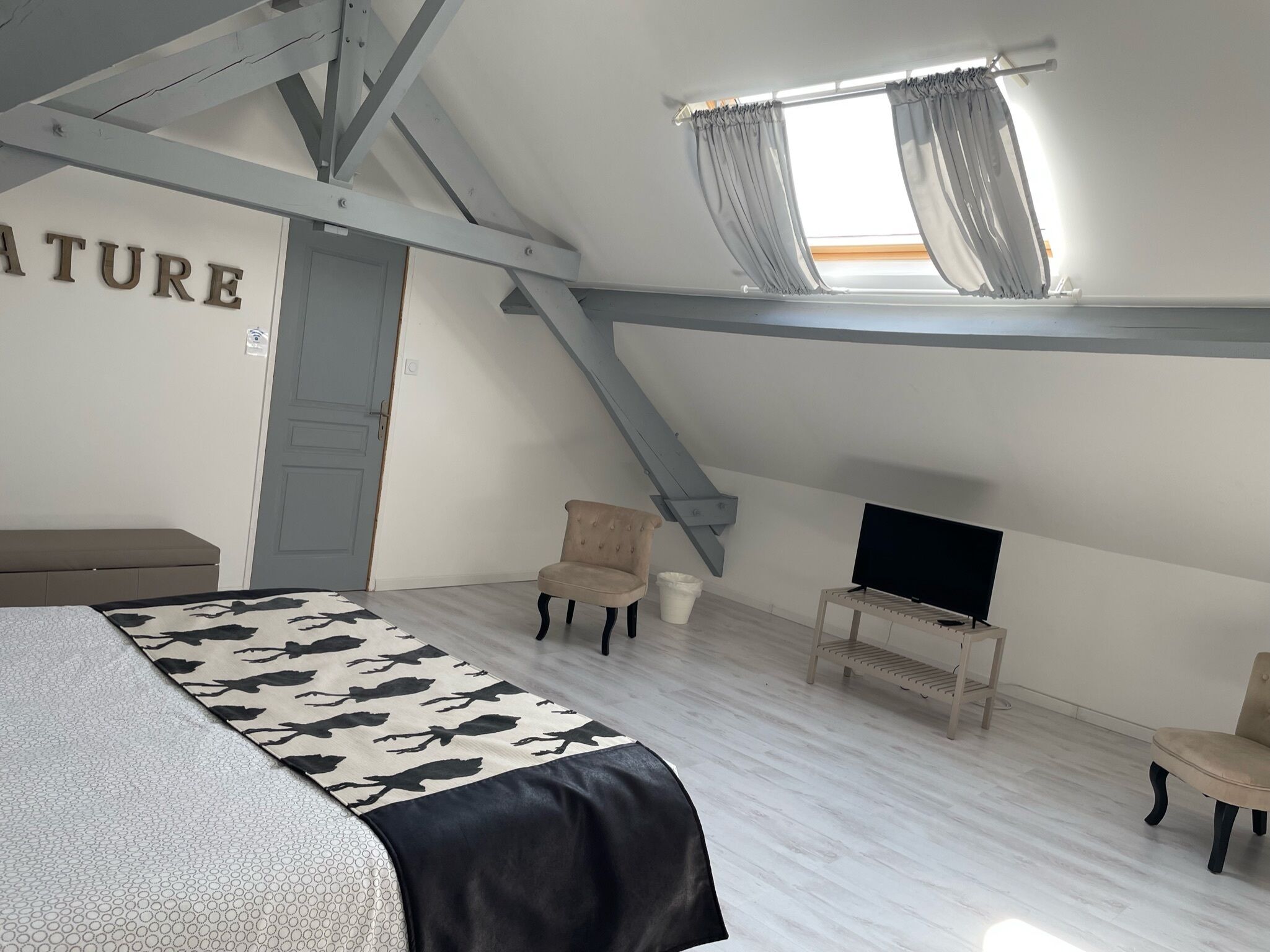 Une chambre à coucher avec un lit, deux chaises, un téléviseur et une fenêtre avec des rideaux.