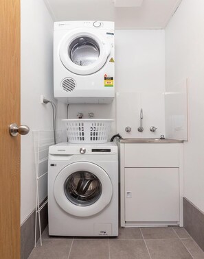 A compact laundry area with a front-loading washer and dryer, a small sink, and a basket for laundry.