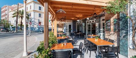 An outdoor cafe with wooden tables and chairs, a covered seating area, and a view of the street.
