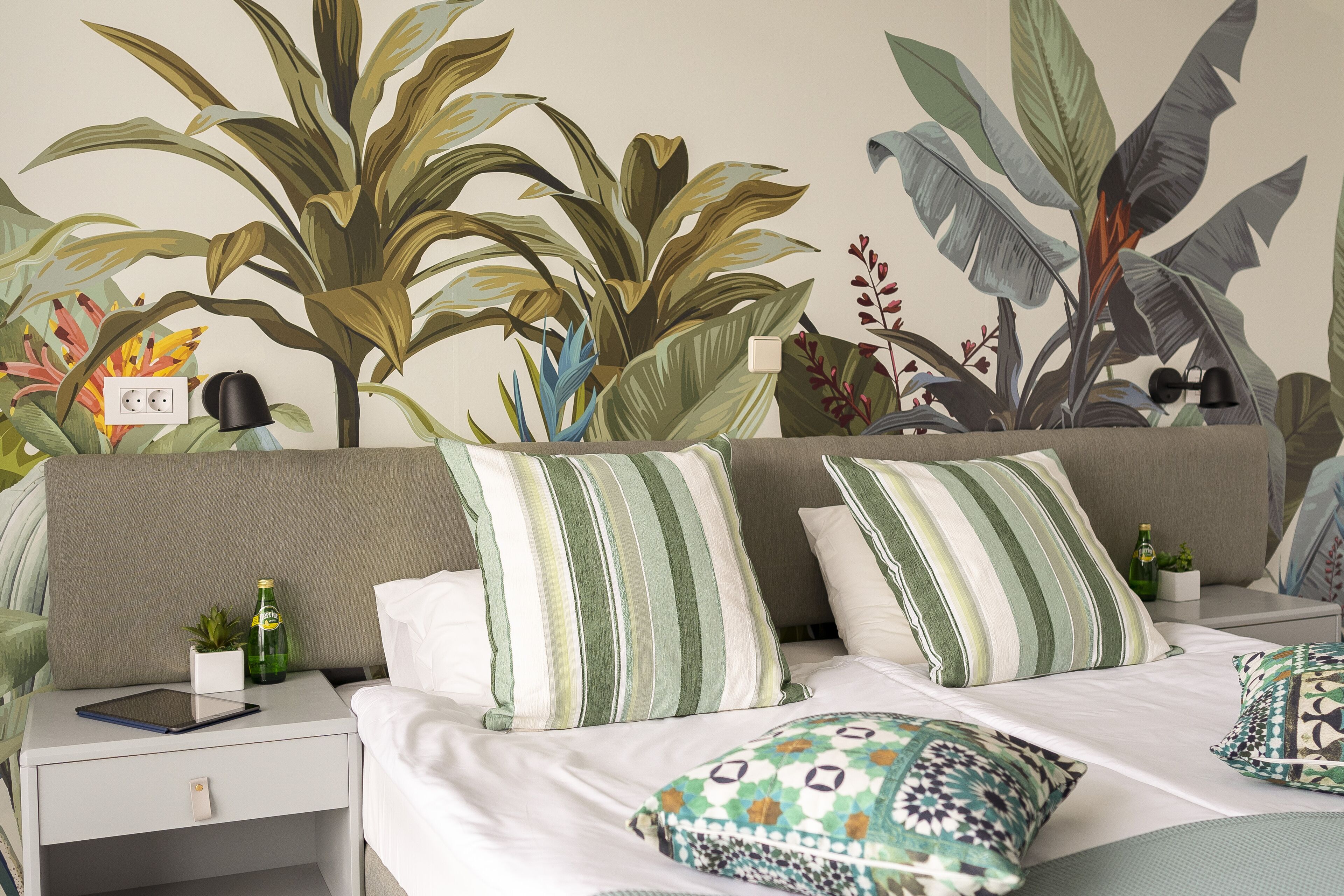 A bedroom with a bed, two nightstands, a wall mural, and a small potted plant.