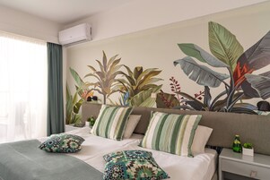 Habitación de hotel con cama, almohadas, mesita de noche, aire acondicionado instalado en la pared y un ventanal con cortinas.