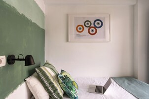 Un dormitorio ordenado con una cama, una computadora portátil y una lámpara de pared.