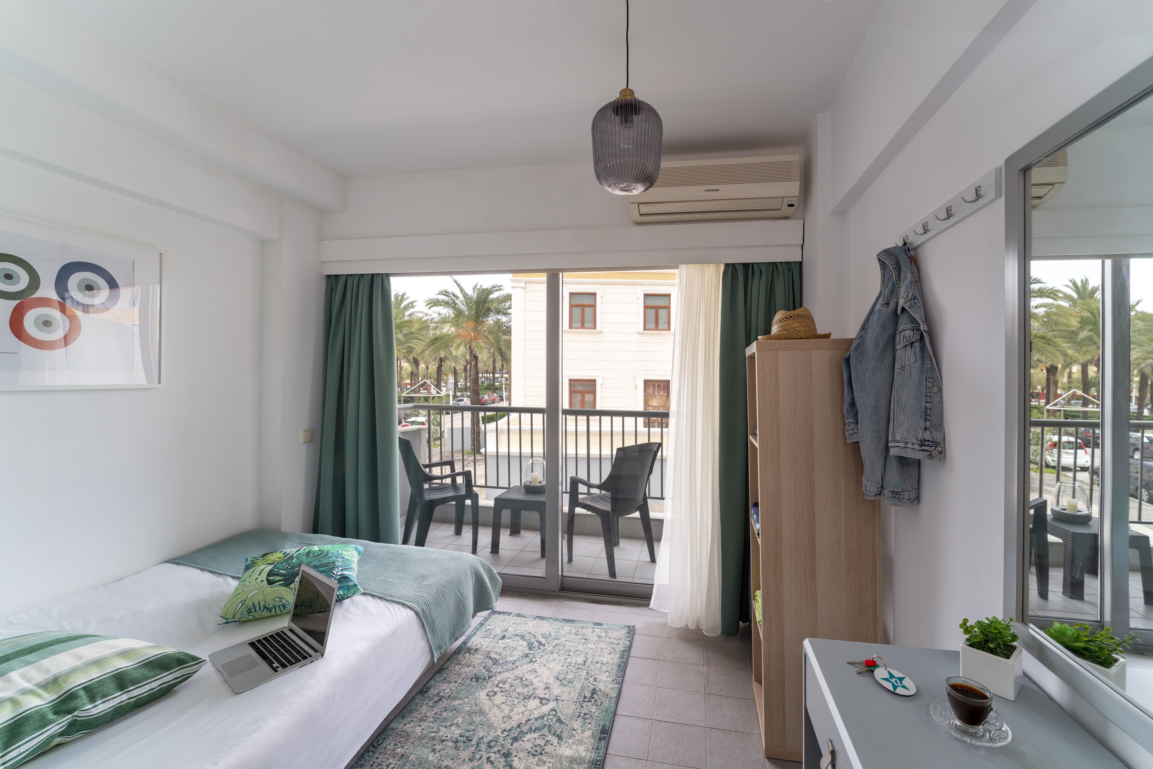 Een moderne hotelkamer met een balkon, een bed met een laptop, een klein tafeltje met een kopje en uitzicht op buiten.