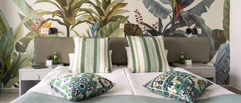 Un dormitorio con una cama, dos mesitas de noche, un sofá y un amplio mural vegetal en la pared.