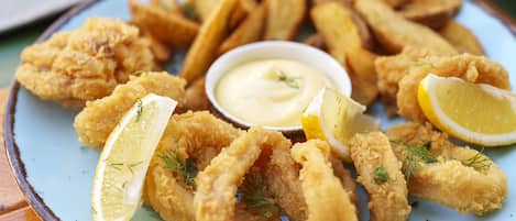A plate of fried calamari and fries with lemon wedges and a small bowl of dipping sauce.