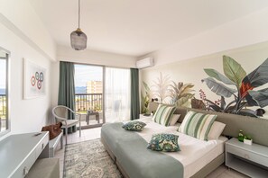 A modern bedroom with a large bed, a desk, and a balcony with a view.