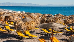A beach with rows of sun loungers and thatched umbrellas.