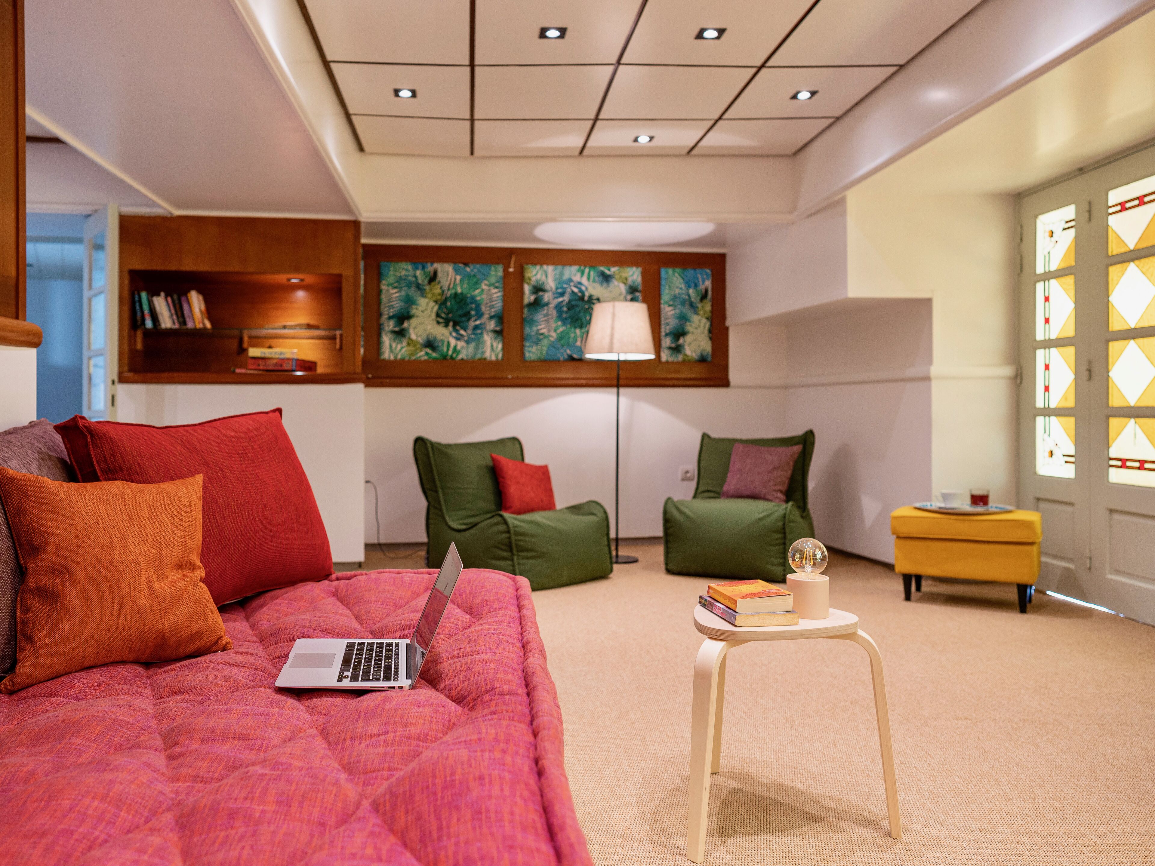 Un dormitorio moderno con cama, dos sillas verdes, una mesita con libros y un ordenador portátil sobre la cama.