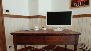 Ett skrivbord i trä med en datorskärm, böcker och ett glas.