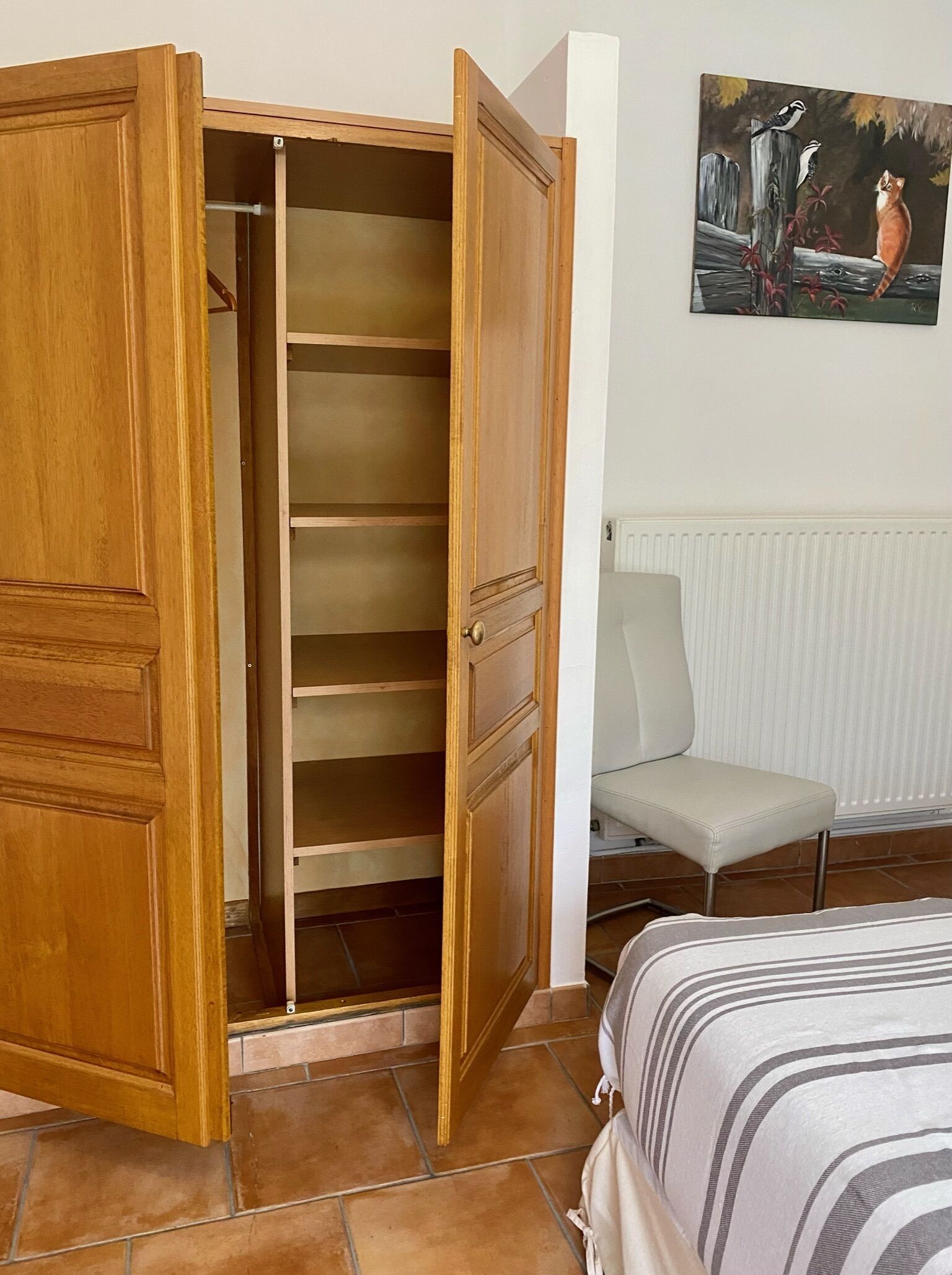 Een houten garderobe met meerdere planken, een stoel en een schilderij aan de muur.