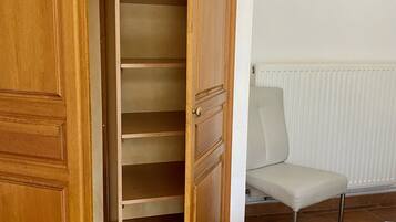 Een houten garderobe met meerdere planken, een stoel en een schilderij aan de muur.