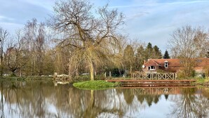 A tranquil lakeside setting with a wooden dock extending into the water, surrounded by leafless trees and a small house with a red roof.