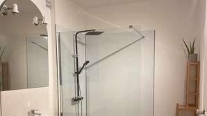 A modern bathroom with a glass-enclosed shower, a vanity with a sink, and a mirror.