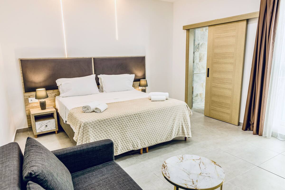 Une chambre bien rangée, avec un lit, des tables de chevet, un canapé et une petite table ronde.
