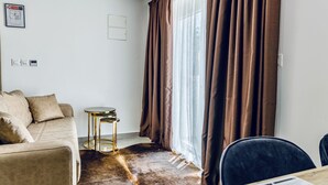 A modern living room with a sofa, a small round table, and a dining table. - The Mike Hotel (Cospicua)