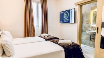 A hotel room with two beds, a TV mounted on the wall, and a bathroom visible through an open door.