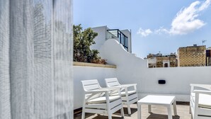 A rooftop terrace with white outdoor furniture, including chairs and a table, and a view of surrounding buildings. - The Mike Hotel (Cospicua)