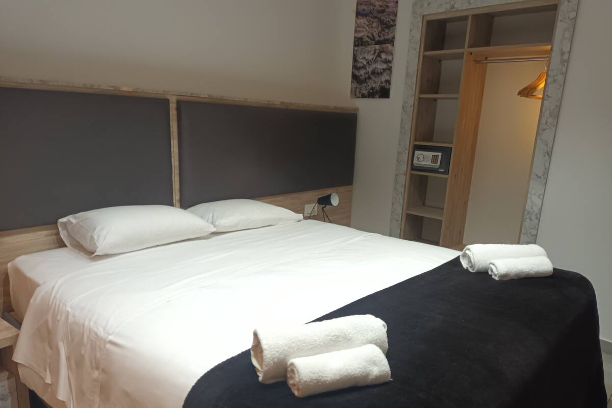 Un lit bien fait, avec des draps blancs et deux serviettes enroulées posées sur le lit.