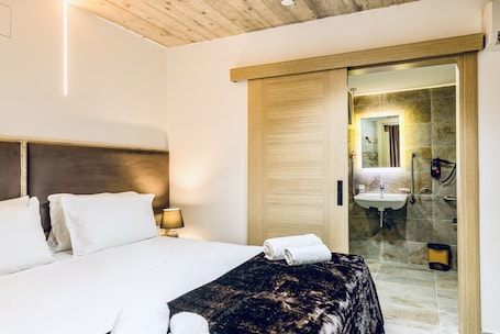 A hotel room with a bed, a nightstand, a lamp, a robe, and a bathroom visible through an open door.