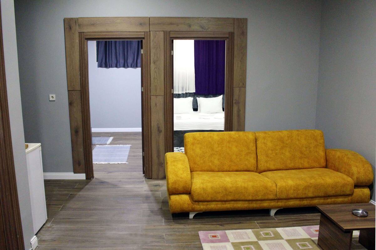 A living room with a yellow sofa, wooden door frame, and a view through the door.