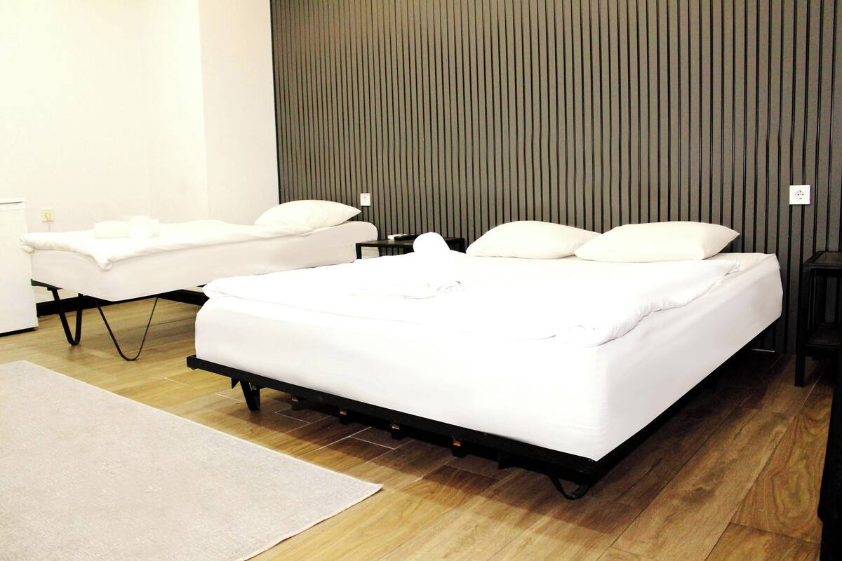 A modern hotel room with a large bed, two bedside tables, and a wooden floor.