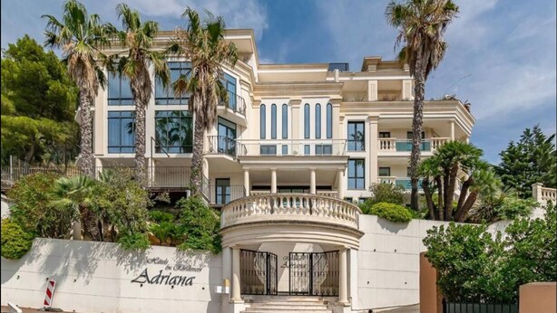 Ein mehrstöckiges Hotel mit klassischer Fassade, Palmen und einem verschlossenen Eingang.
