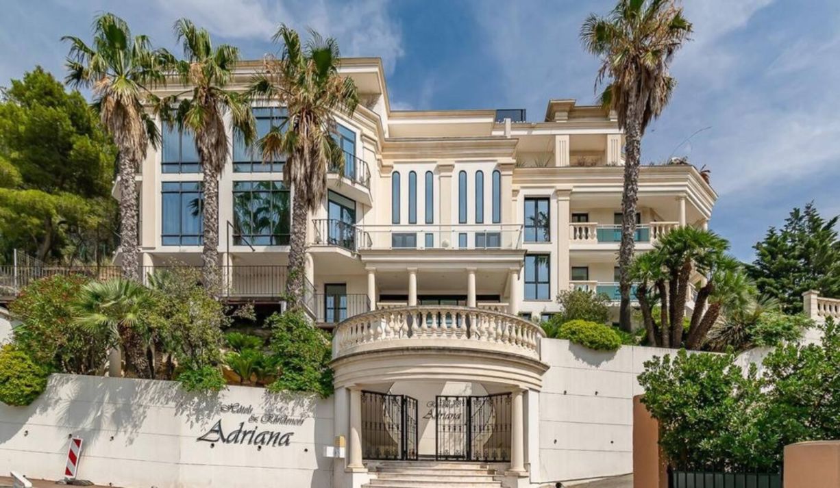 Ein mehrstöckiges Hotel mit klassischer Fassade, Palmen und einem verschlossenen Eingang.