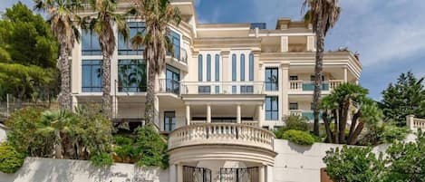 A multi-story hotel with a classical facade, palm trees, and a gated entrance.